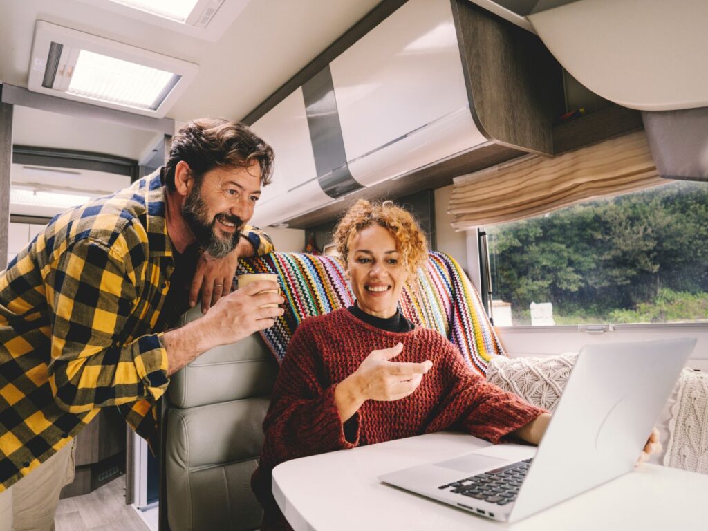 Couple smiling and sat inside campervan, using laptop