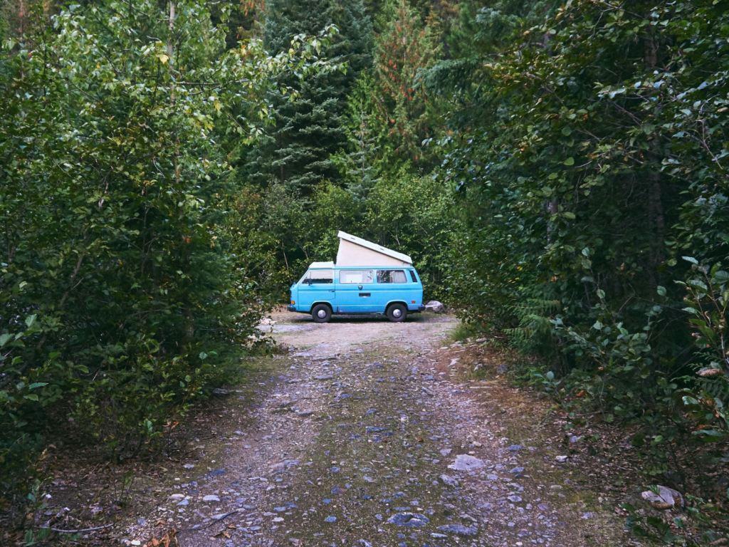 Blue campervan with roof extension, parked in a clearing in forrest