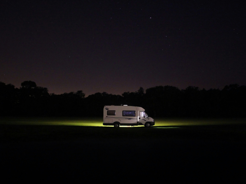 Campervan with light coming from it, parked in a field at night 